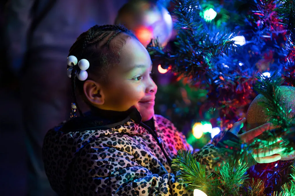 A young girl smiling at the colored lights on a Christmas tree