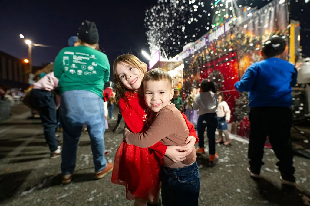 Two children hugging as snow falls on Commerce Street