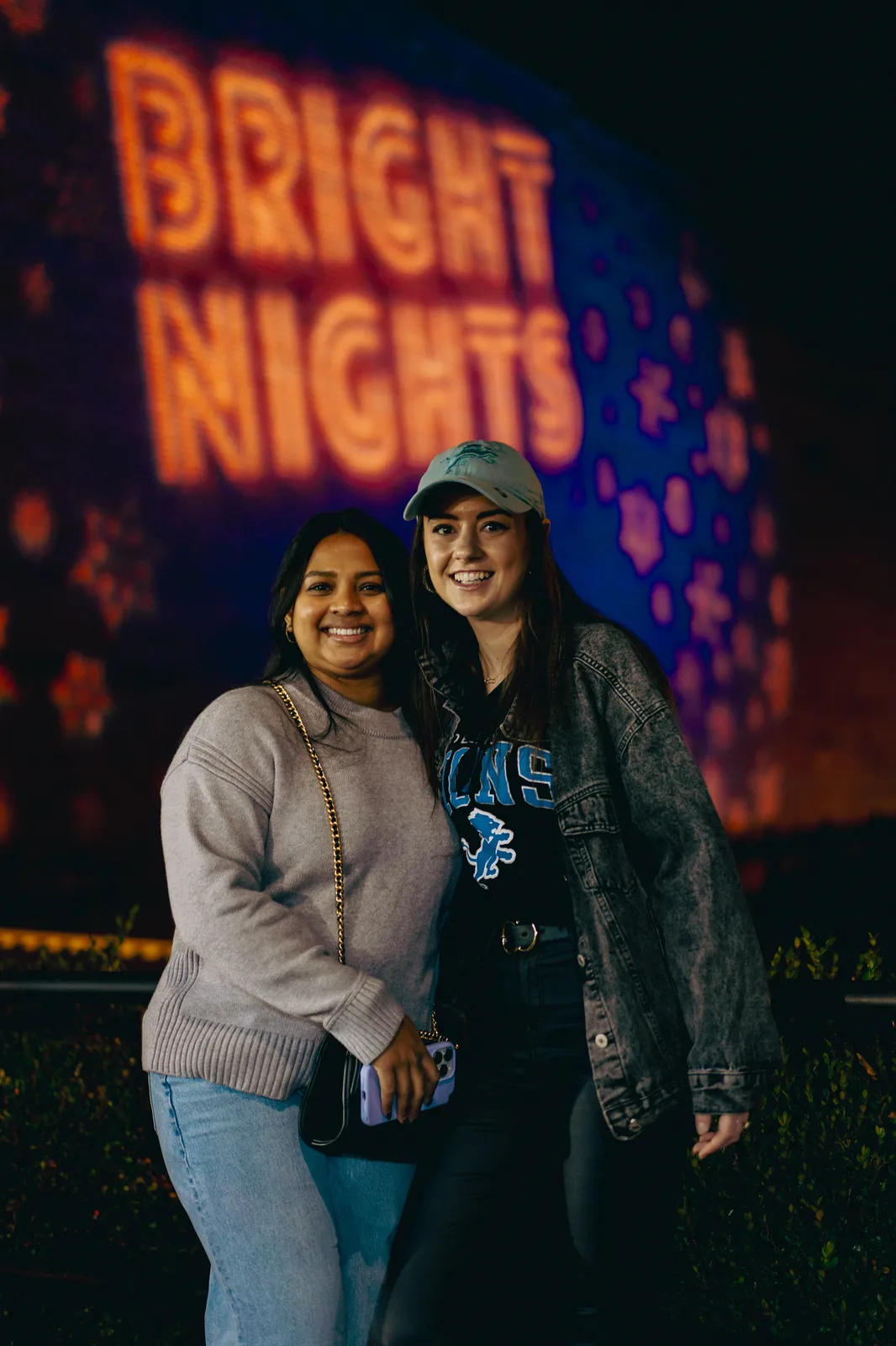 Two friends posing in front of the Bright Nights sign projected on a downtown building