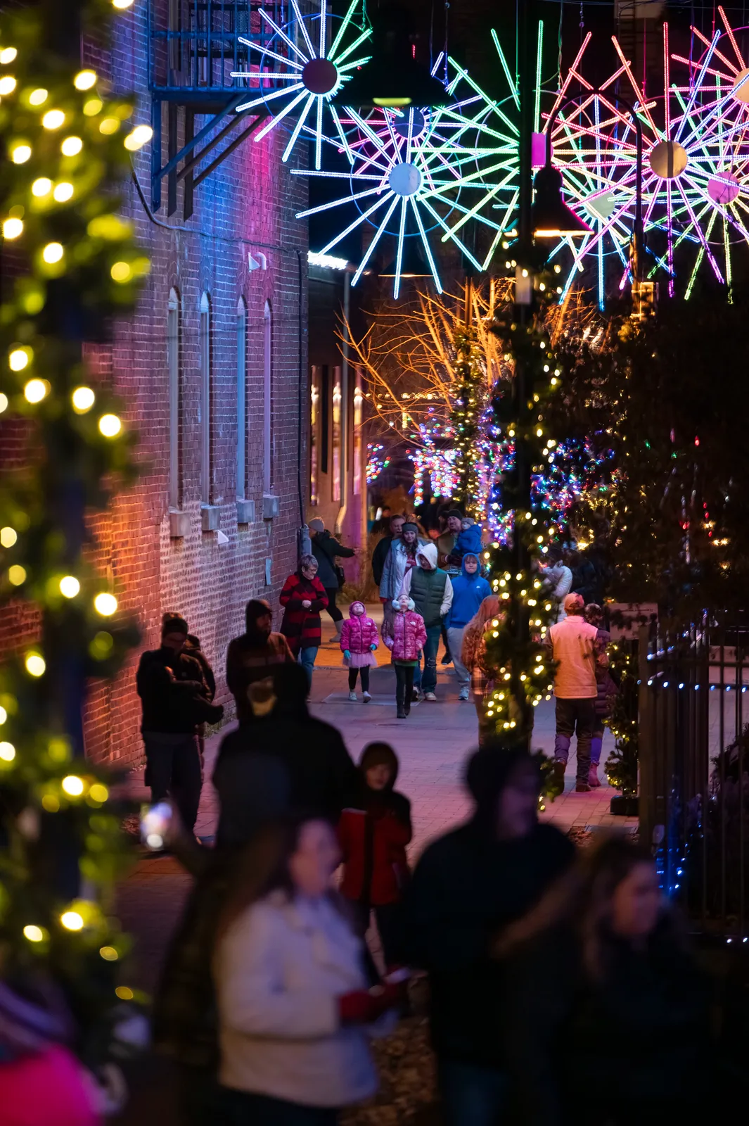 Families strolling beneath glowing starburst light sculptures on a downtown street